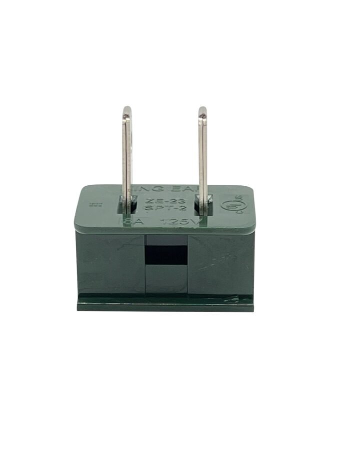 A small, green rectangular electrical component with two vertical metal prongs on top, resembling those used in professional Christmas lights. There are some markings and symbols on the surface. The component is isolated against a white background.