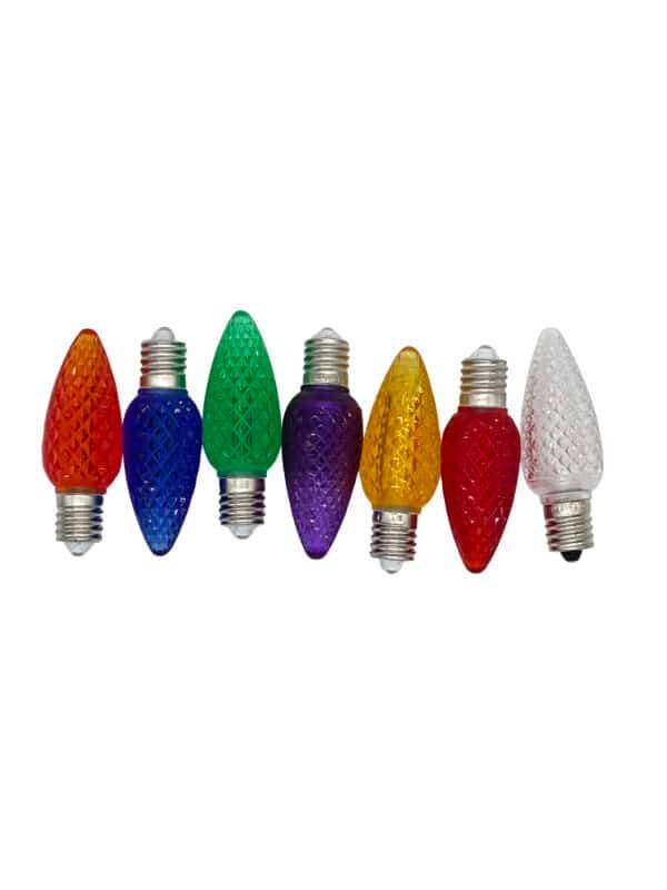 A row of seven faceted LED light bulbs is displayed, ranging in colors: red, orange, blue, green, purple, yellow, and clear. Ideal for commercial Christmas lighting or outdoor Christmas lights setups, the bulbs feature a textured surface and silver screw bases.